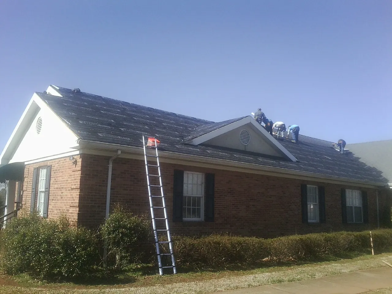 Crew tearing shingles off a brick ranch roof with a ladder set — Emergency Roof Repair work by our crew in South Deerfield