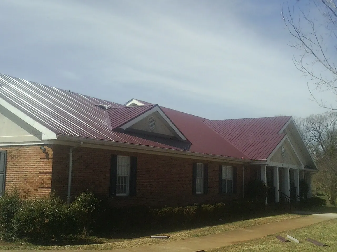 Red metal roof with gabled entries on a long brick building, from a Hail Damage Roof Repair job in South Deerfield