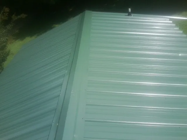 New green metal panels meeting at the ridge of a roof — Flat Roof Repair work by our crew in South Deerfield