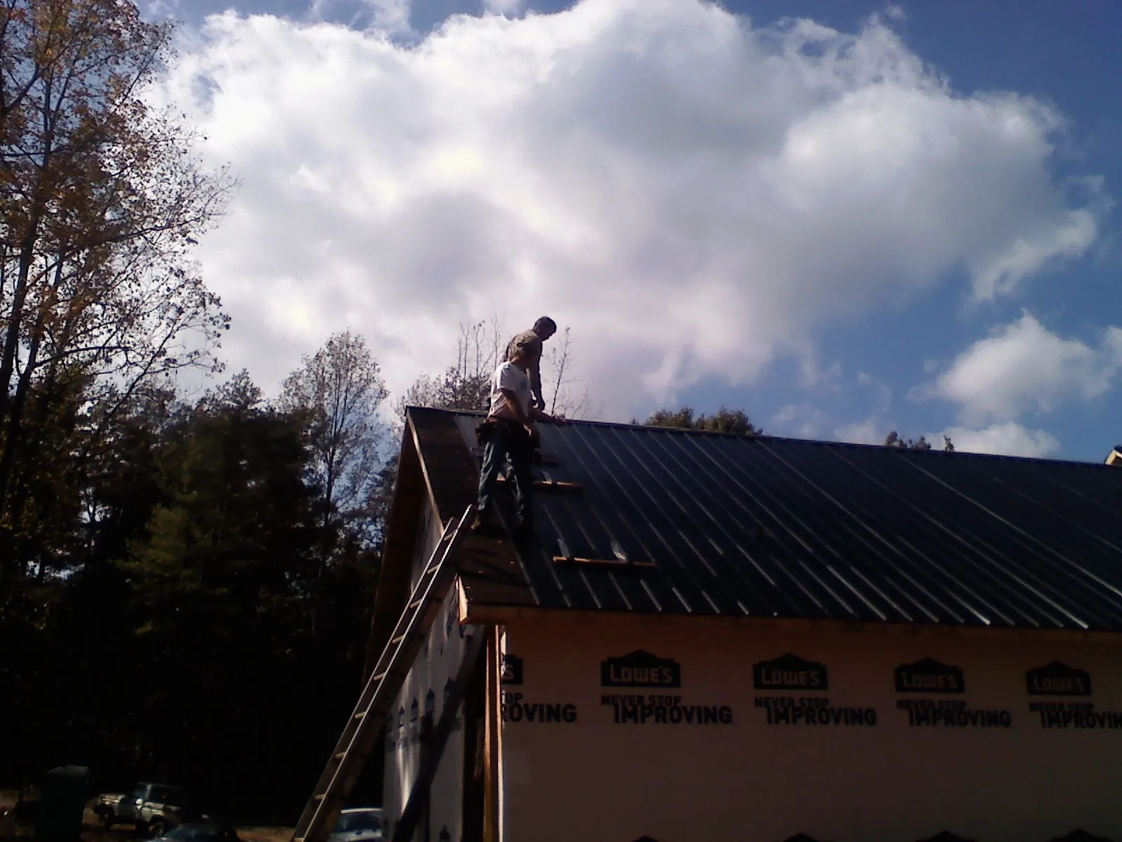 Roofer fastening dark metal panels high against a cloudy sky, from a Roof Inspection job in South Deerfield