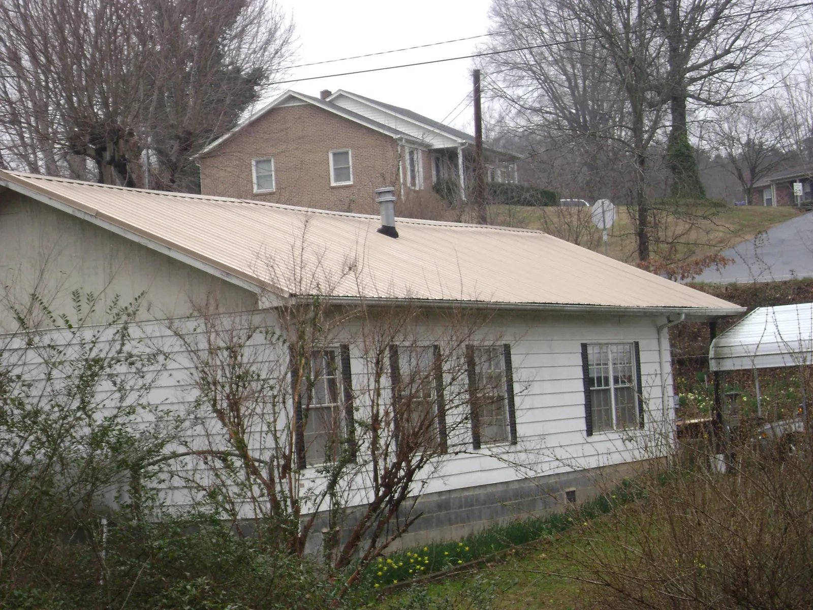 Tan metal roof on a white sided house set into a hillside — Commercial Roofing by Roofing Brothers in South Deerfield